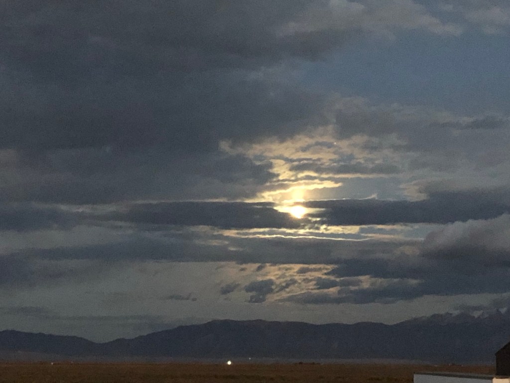 moonlight behind clouds and a mountain range silhouetted on the horizon