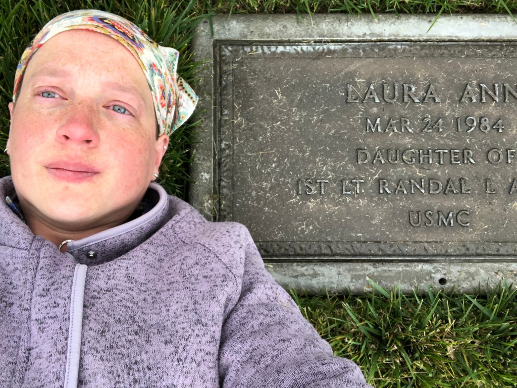 a person laying next to a headstone with the words "Laura Ann March 24 1984. Daughter of 1st Lt. Randal L. Alger, USMC"
