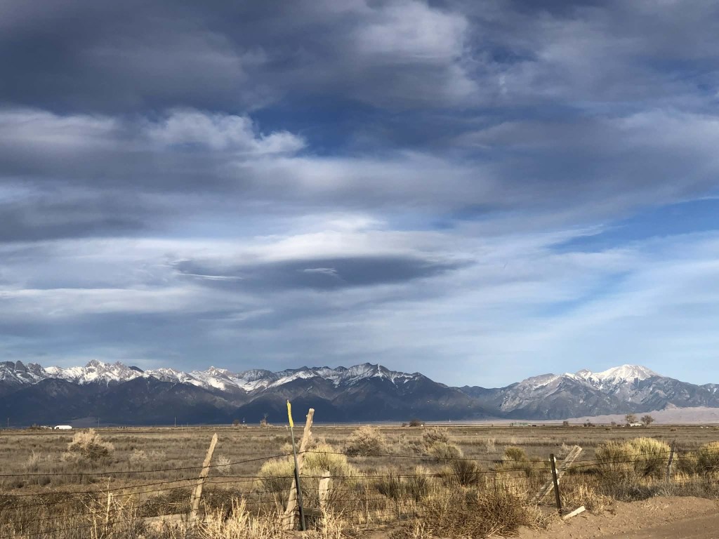 mountains in the distance, below a cloudy sky and above an open field.